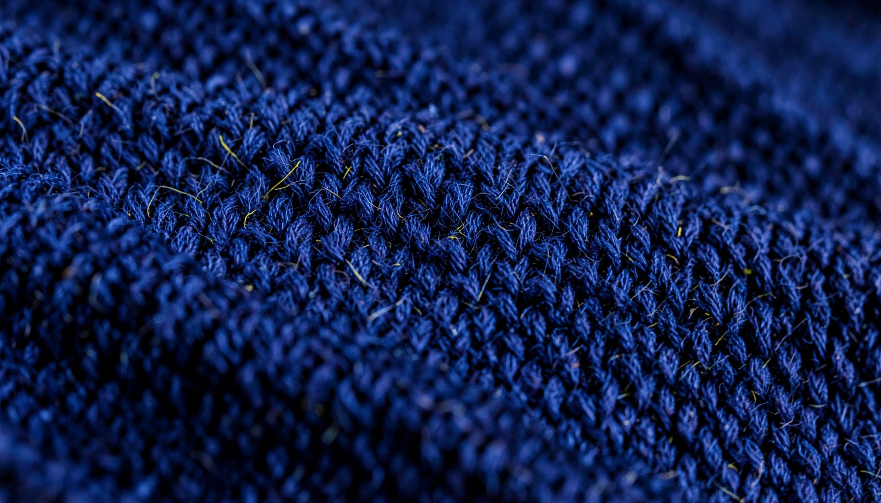 Extreme close-up photograph of tightly woven wool fabric in deep navy blue, showing the rich texture of individual fibers and subtle variations in tone across the surface.